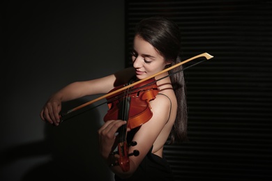 Beautiful young woman playing violin in dark room