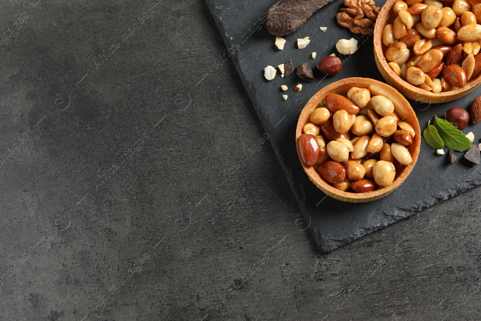 Photo of Tartlets with caramelized nuts on black table, top view and space for text. Delicious dessert