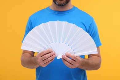 Photo of Man holding hand fan on orange background, closeup