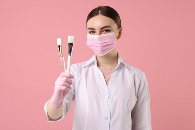 Photo of Cosmetologist with cosmetic brushes on pink background