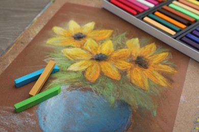 Photo of Beautiful drawing of yellow flowers and pastels on table, closeup
