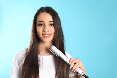 Happy woman using hair iron on color background. Space for text