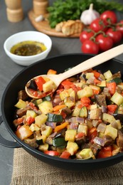 Photo of Delicious ratatouille and spoon in baking dish on table, closeup