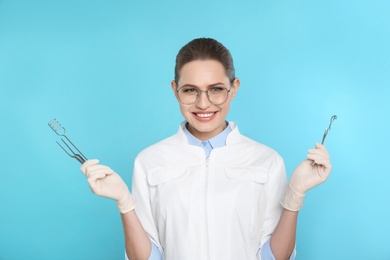 Photo of Female dentist holding professional tools on color background