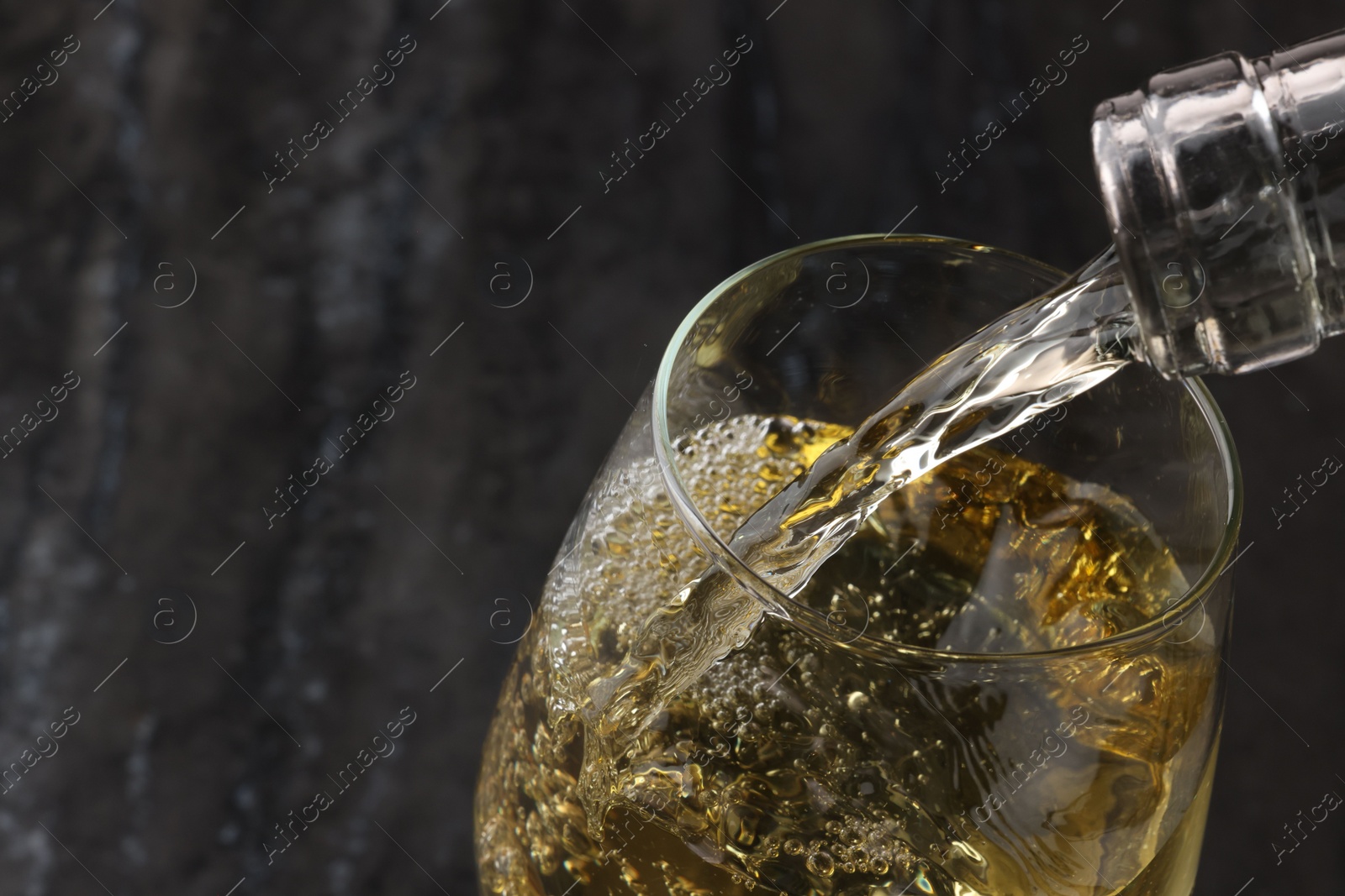Photo of Pouring tasty aromatic wine in glass against blurred background, closeup. Space for text