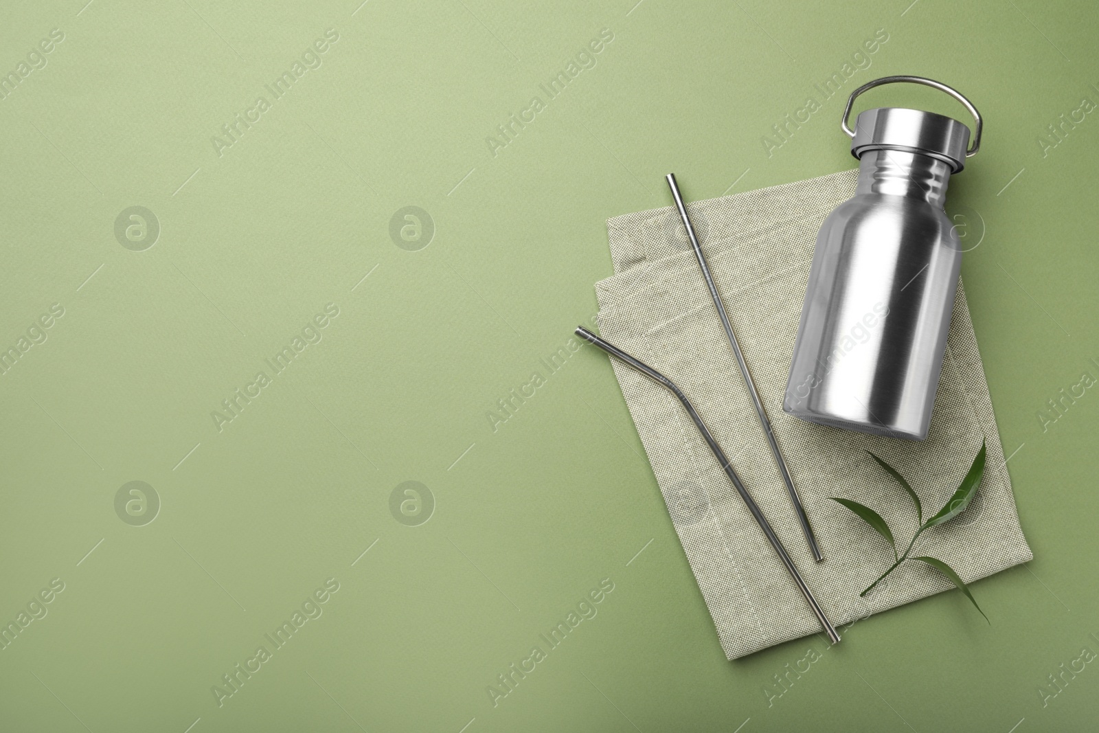 Photo of Bottle,metal straws and space for text on green background, flat lay. Eco friendly products