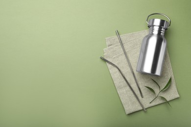 Photo of Bottle,metal straws and space for text on green background, flat lay. Eco friendly products