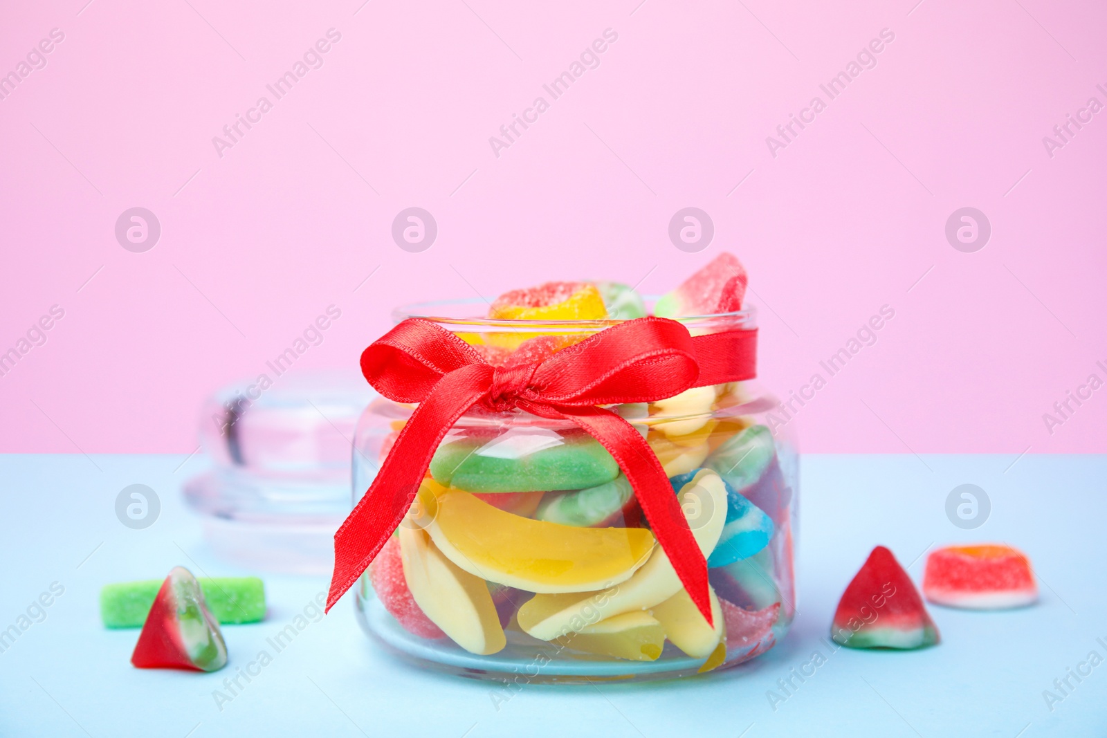Photo of Glass jar with tasty colorful jelly candies on light blue table against pink background
