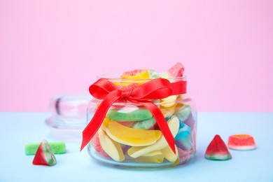 Photo of Glass jar with tasty colorful jelly candies on light blue table against pink background