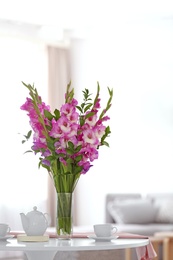 Photo of Vase with beautiful pink gladiolus flowers on wooden table in living room