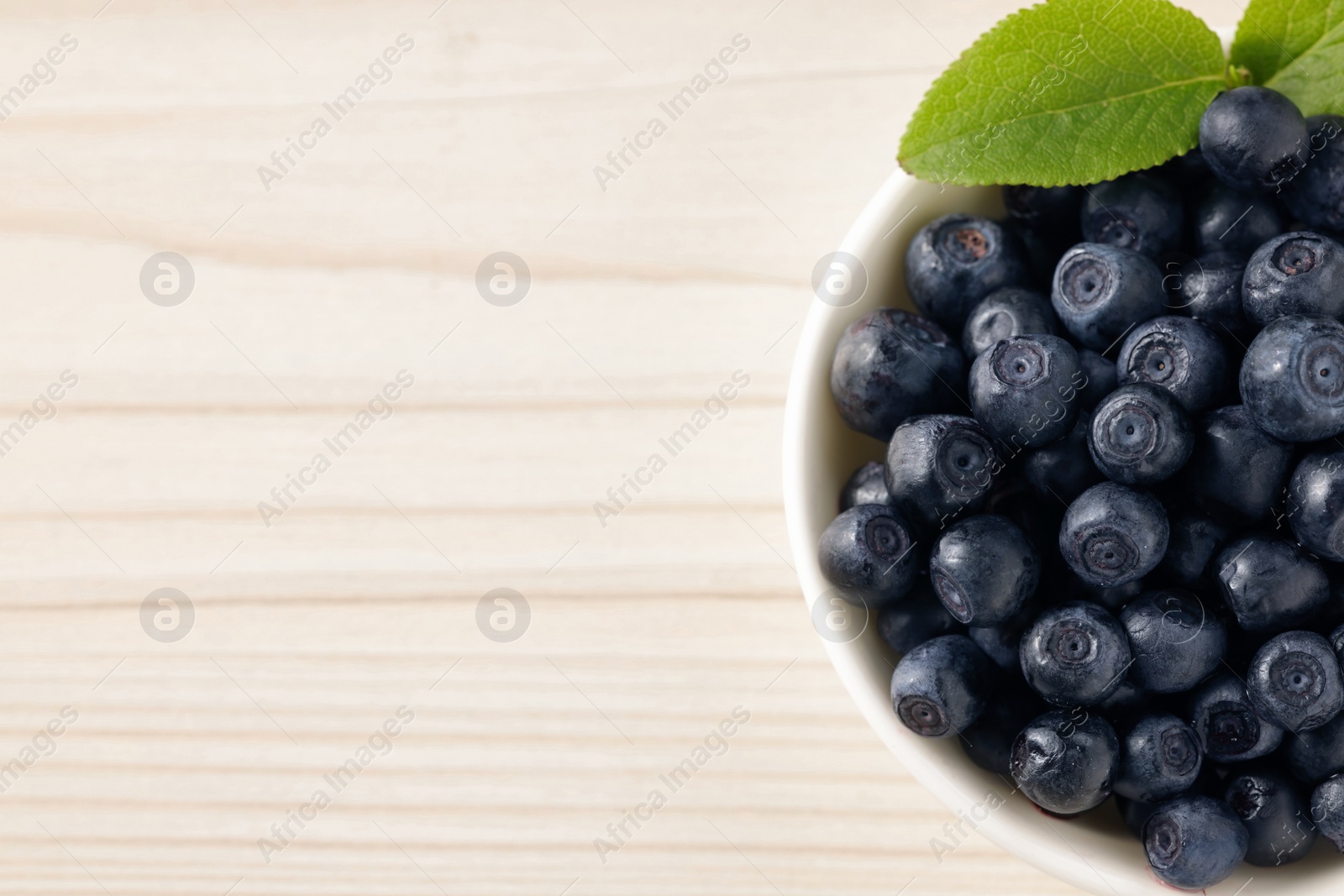 Photo of Tasty fresh bilberries with leaves in bowl on white table, top view. Space for text