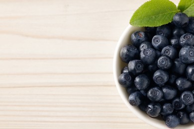 Tasty fresh bilberries with leaves in bowl on white table, top view. Space for text