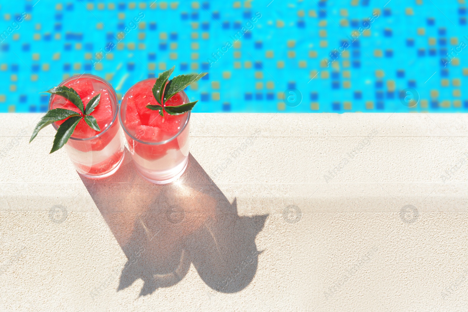 Photo of Refreshing watermelon drink in glasses near swimming pool outdoors, top view. Space for text