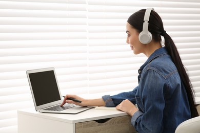 Photo of Woman in headphones studying on laptop indoors. Online translation course