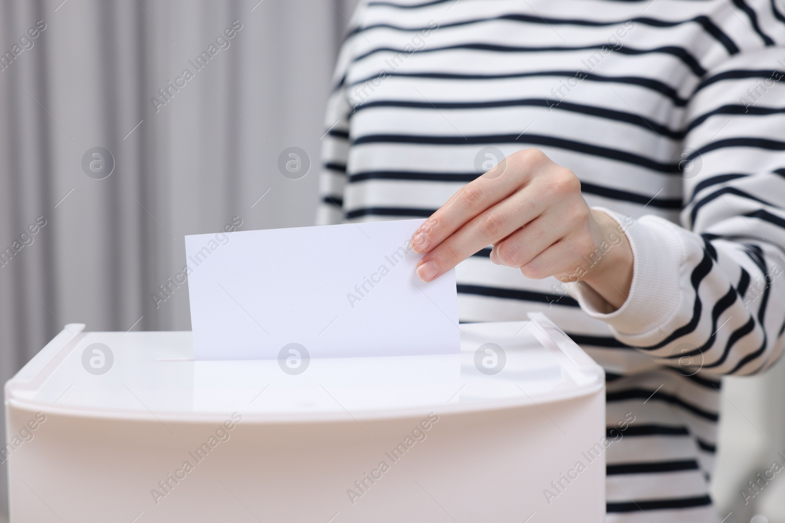 Photo of Woman putting her vote into ballot box on blurred background, closeup