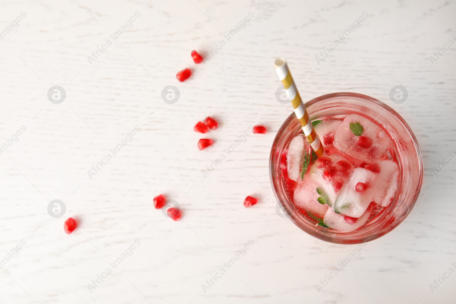 Photo of Tasty cocktail with pomegranate ice cubes and seeds on wooden background, top view. Space for text