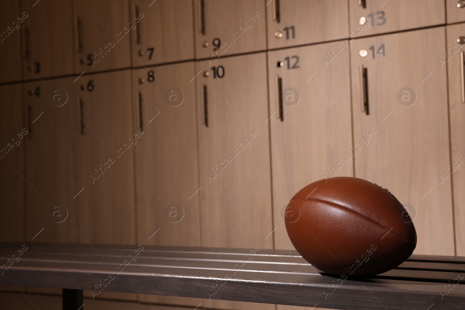 Photo of Leather American football ball on wooden bench in locker room. Space for text