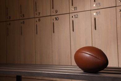 Photo of Leather American football ball on wooden bench in locker room. Space for text