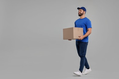 Happy young courier with parcel on grey background, space for text