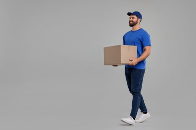 Photo of Happy young courier with parcel on grey background, space for text