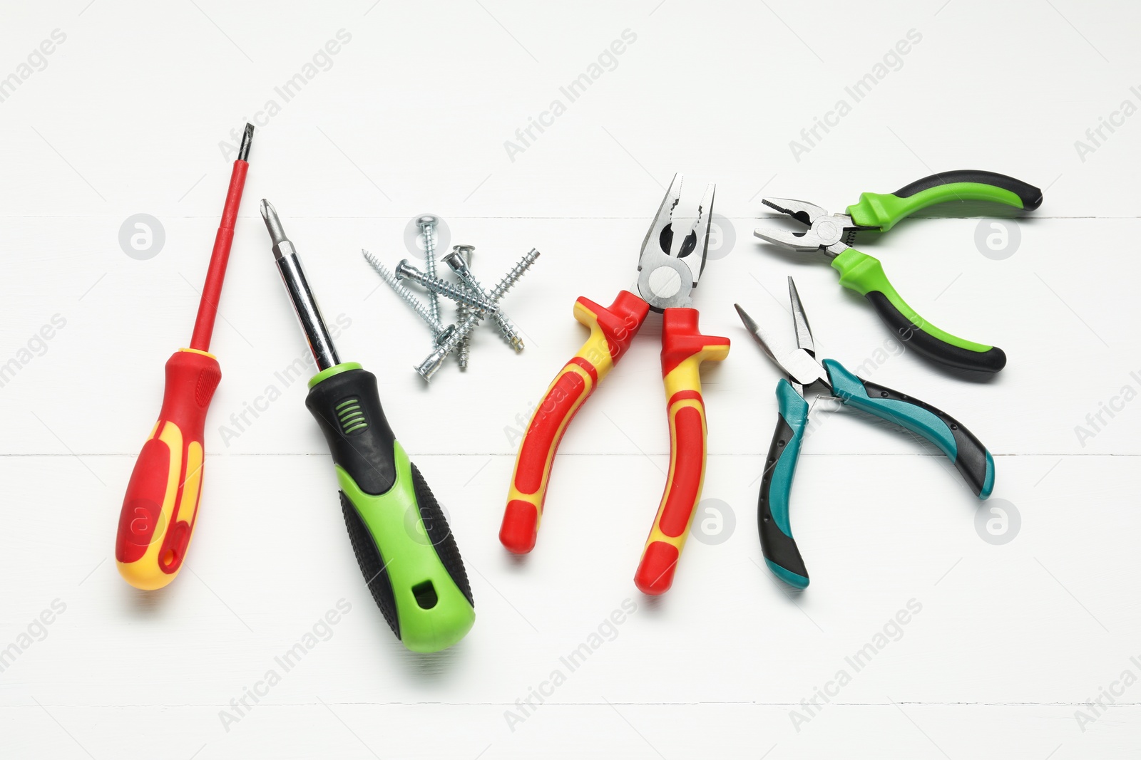 Photo of Pliers, screwdrivers and screws on white wooden table, flat lay