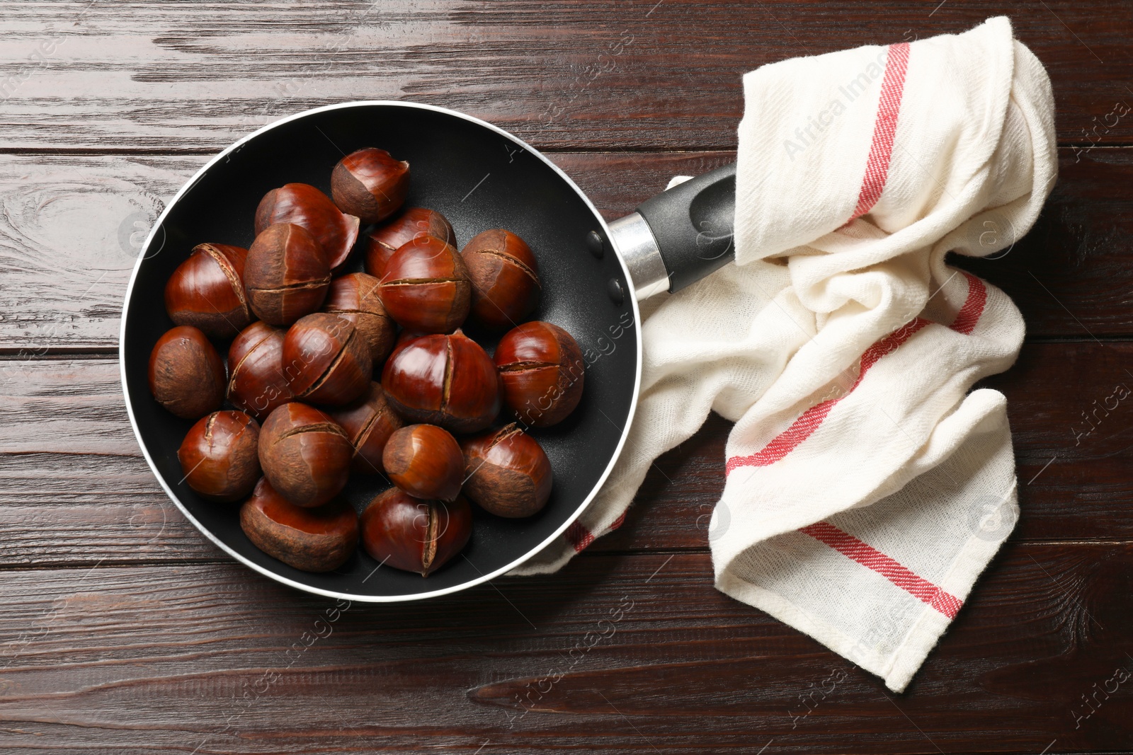 Photo of Roasted edible sweet chestnuts in frying pan on wooden table, top view