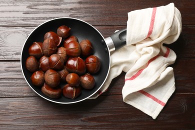 Roasted edible sweet chestnuts in frying pan on wooden table, top view