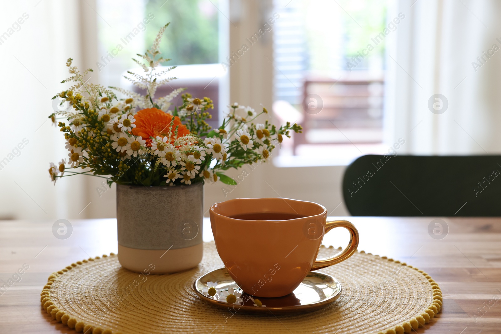 Photo of Cup of delicious chamomile tea and fresh flowers on wooden table in room