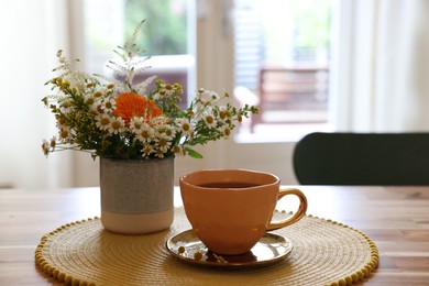 Photo of Cup of delicious chamomile tea and fresh flowers on wooden table in room