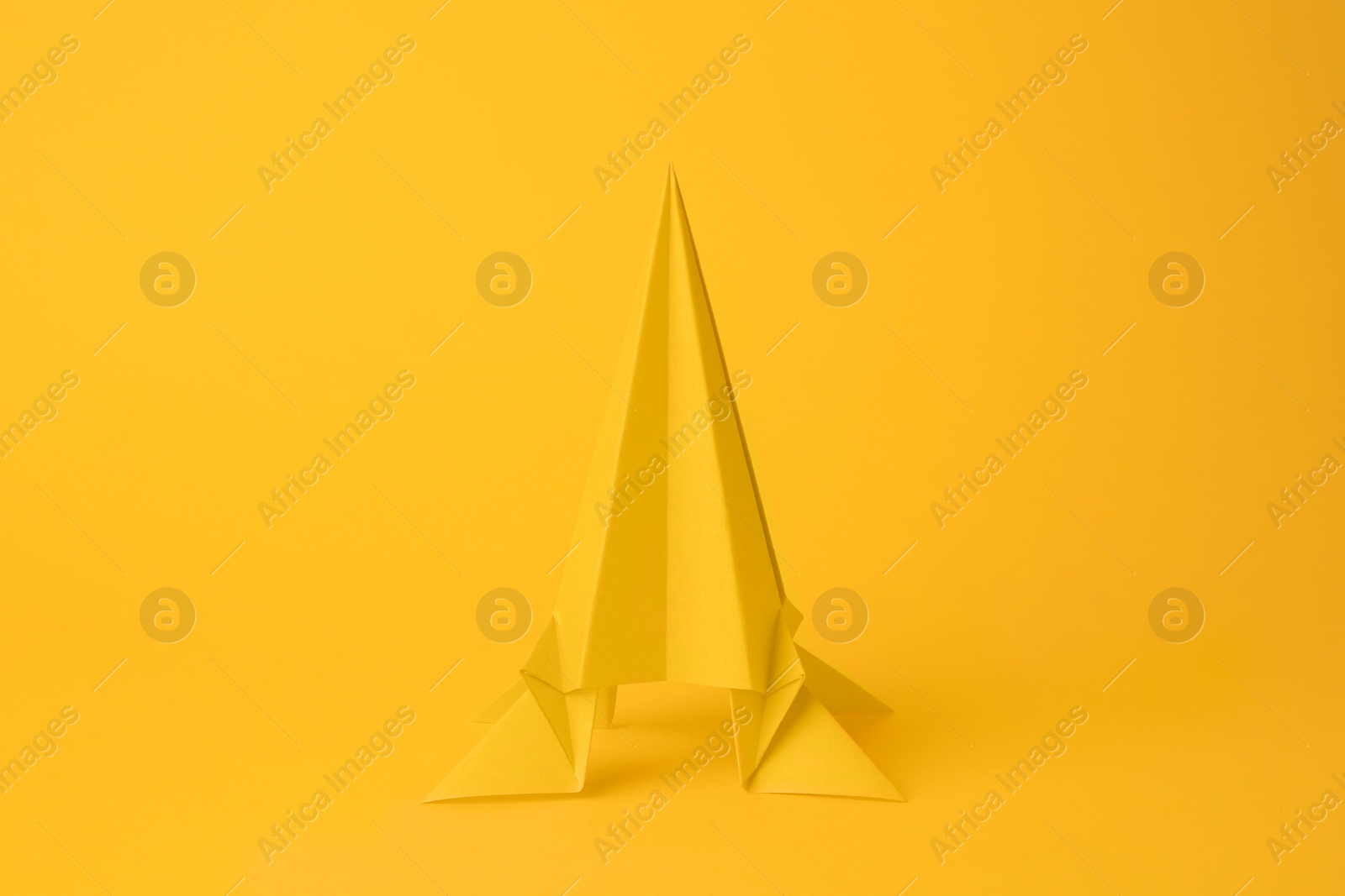 Photo of Origami art. Handmade bright paper rocket on yellow background