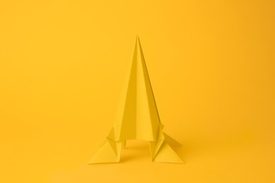 Photo of Origami art. Handmade bright paper rocket on yellow background