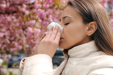 Woman suffering from seasonal pollen allergy near blossoming tree outdoors