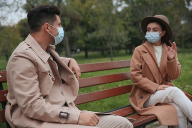 Photo of Man and woman talking on bench in park. Keeping social distance during coronavirus pandemic