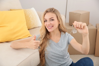 Happy young woman with key from her new house indoors