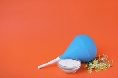 Photo of Enema, flowers and bowl of salt on orange background, space for text. Medical treatment