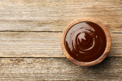 Photo of Tasty barbeque sauce in bowl on wooden table, top view. Space for text