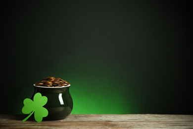 Photo of Pot with gold coins and clover on wooden table against dark background, space for text. St. Patrick's Day