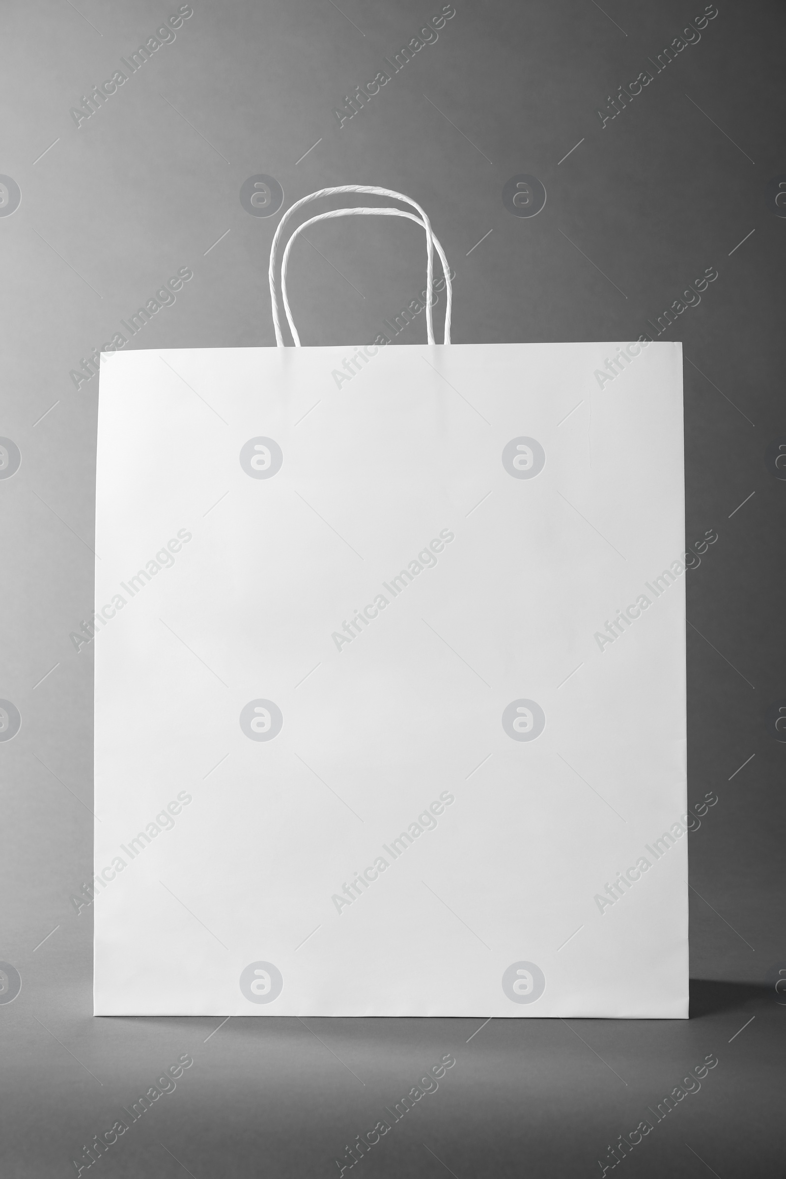 Photo of One white paper bag on grey background. Mockup for design