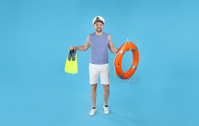 Photo of Happy sailor with orange ring buoy and yellow swim fins on light blue background