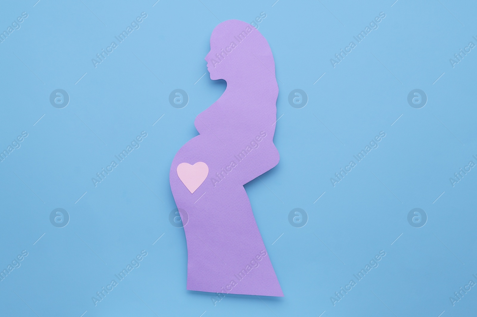 Photo of Pregnant woman with heart on belly on light blue background, top view