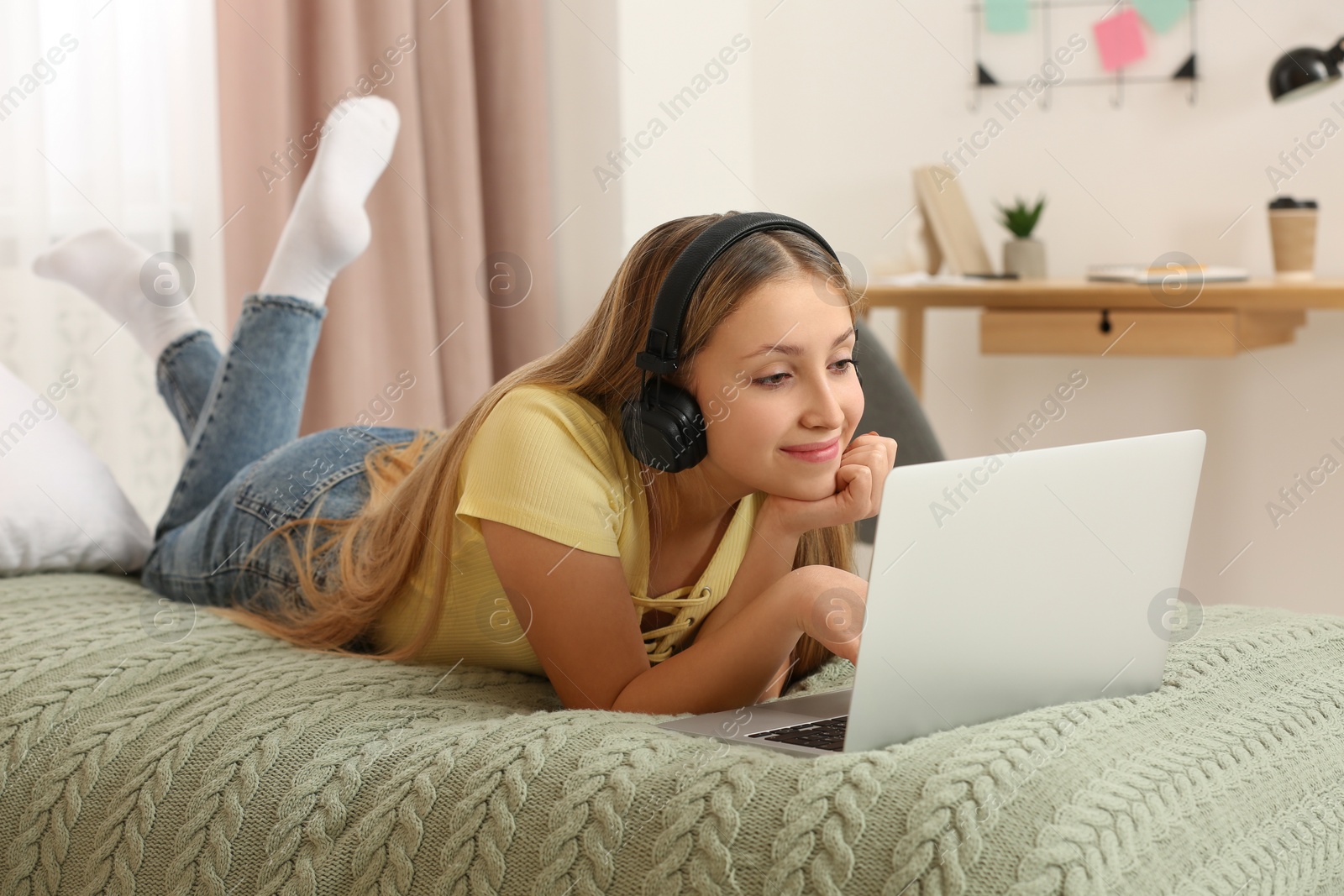 Photo of Teenage girl with headphones using laptop on bed at home