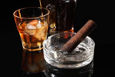 Burnt cigar, ashtray and whiskey on black mirror surface, closeup