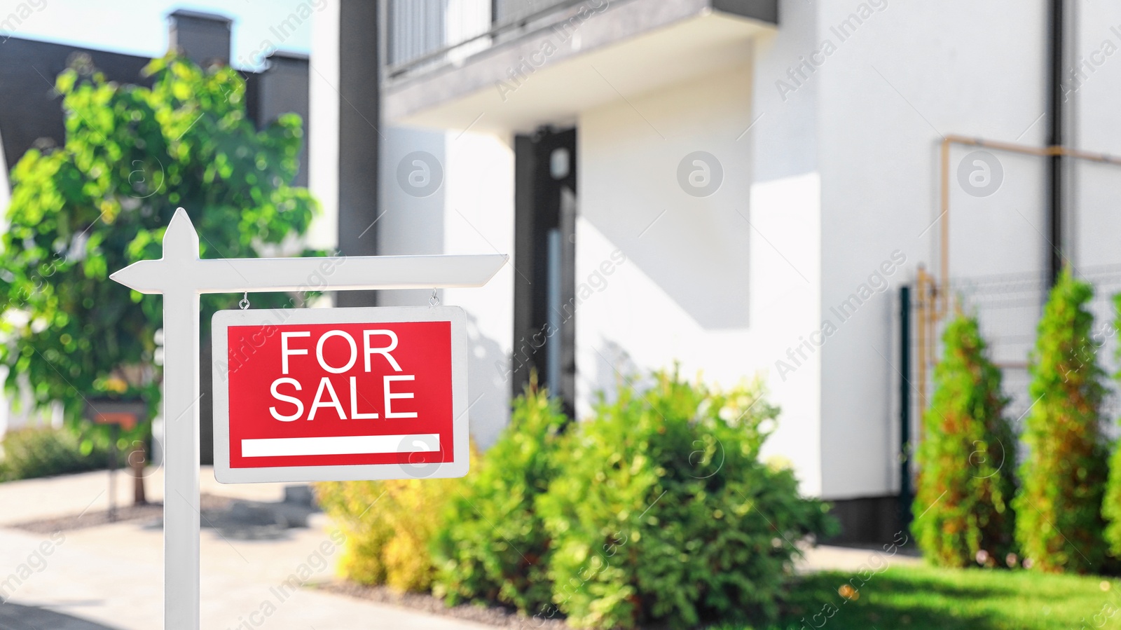 Photo of Red real estate sign near house outdoors on sunny day