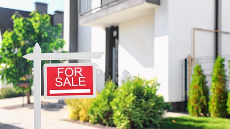 Photo of Red real estate sign near house outdoors on sunny day