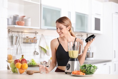 Young woman with tasty healthy smoothie at table in kitchen