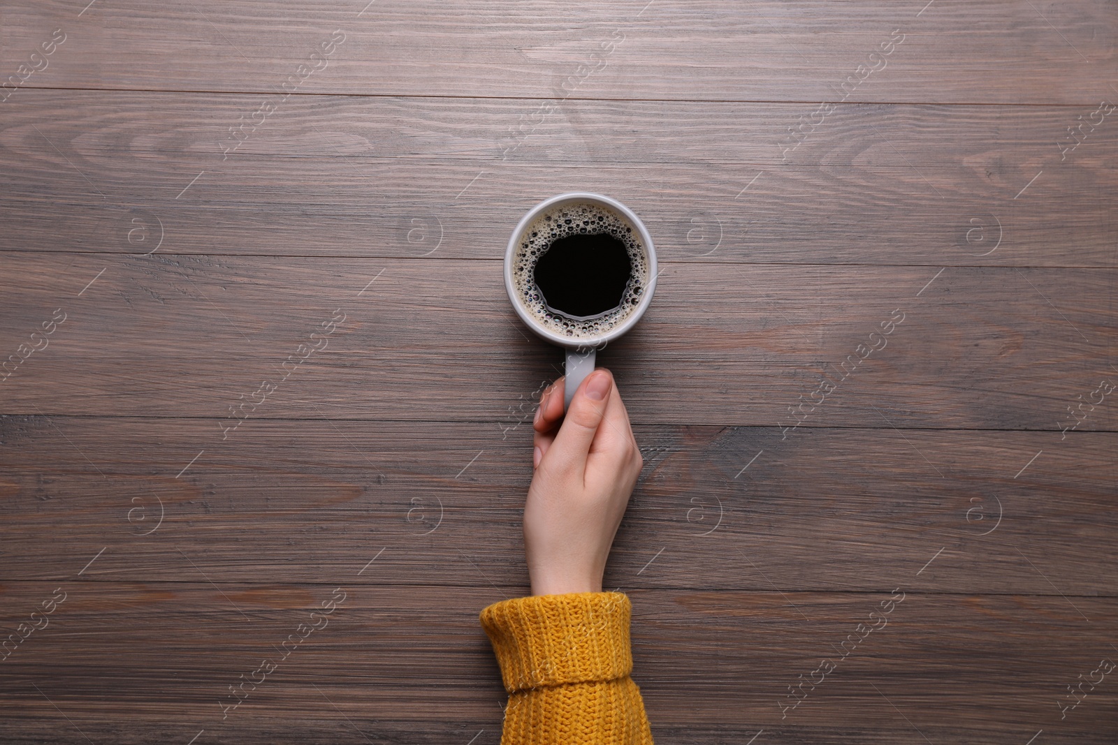 Photo of Woman with cup of coffee at wooden table, top view