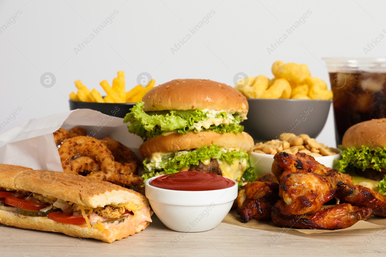 Photo of French fries, burgers and other fast food on wooden table against white background, closeup