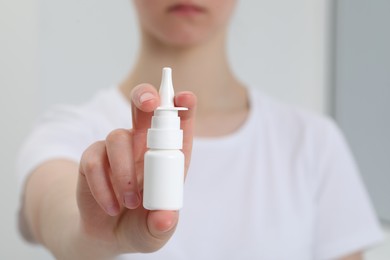 Photo of Woman holding bottle of nasal spray indoors, closeup