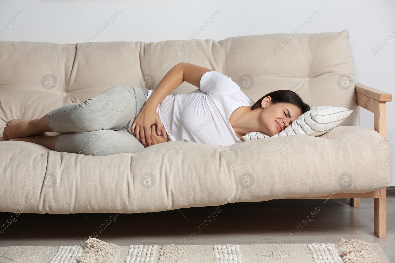 Photo of Young woman suffering from menstrual pain on sofa indoors