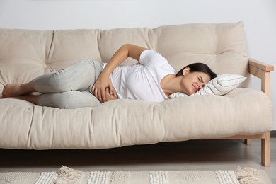 Young woman suffering from menstrual pain on sofa indoors
